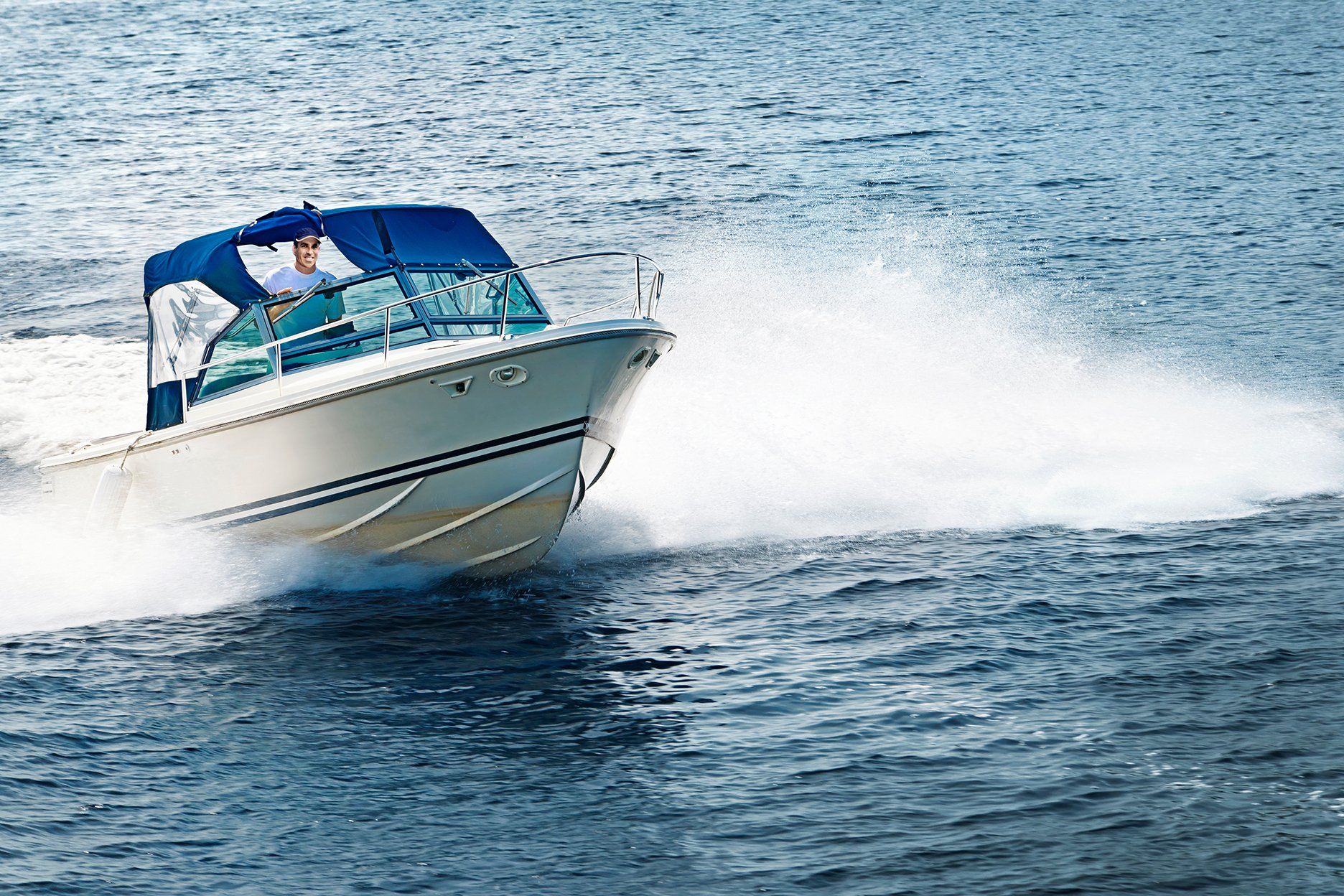 Motorboat speeding on water, creating a white wake. Blue canvas top and a person at the helm.