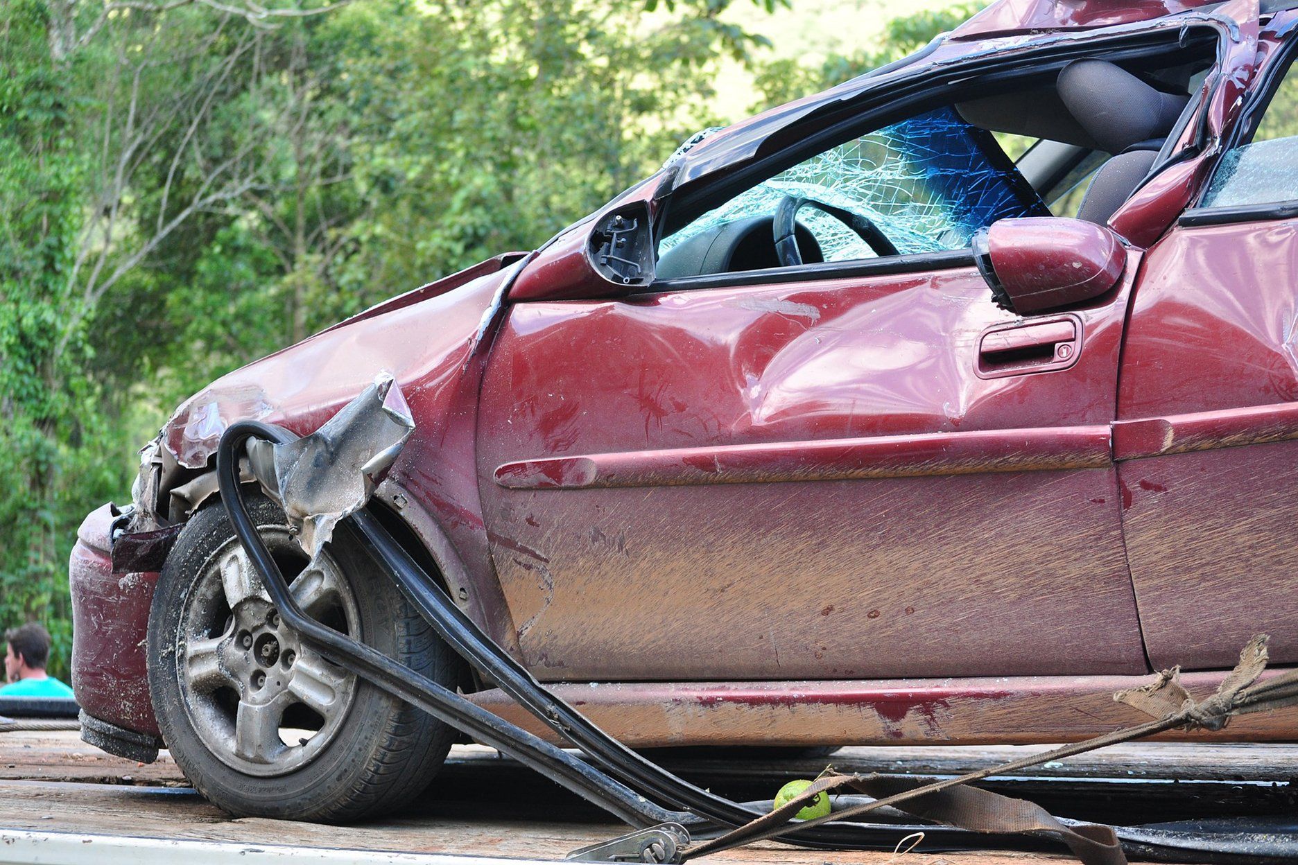 Damaged burgundy car involved in an accident, front end crushed, glass broken, debris present.