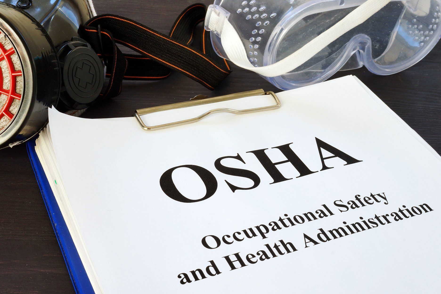 OSHA document on clipboard with respirator and goggles.