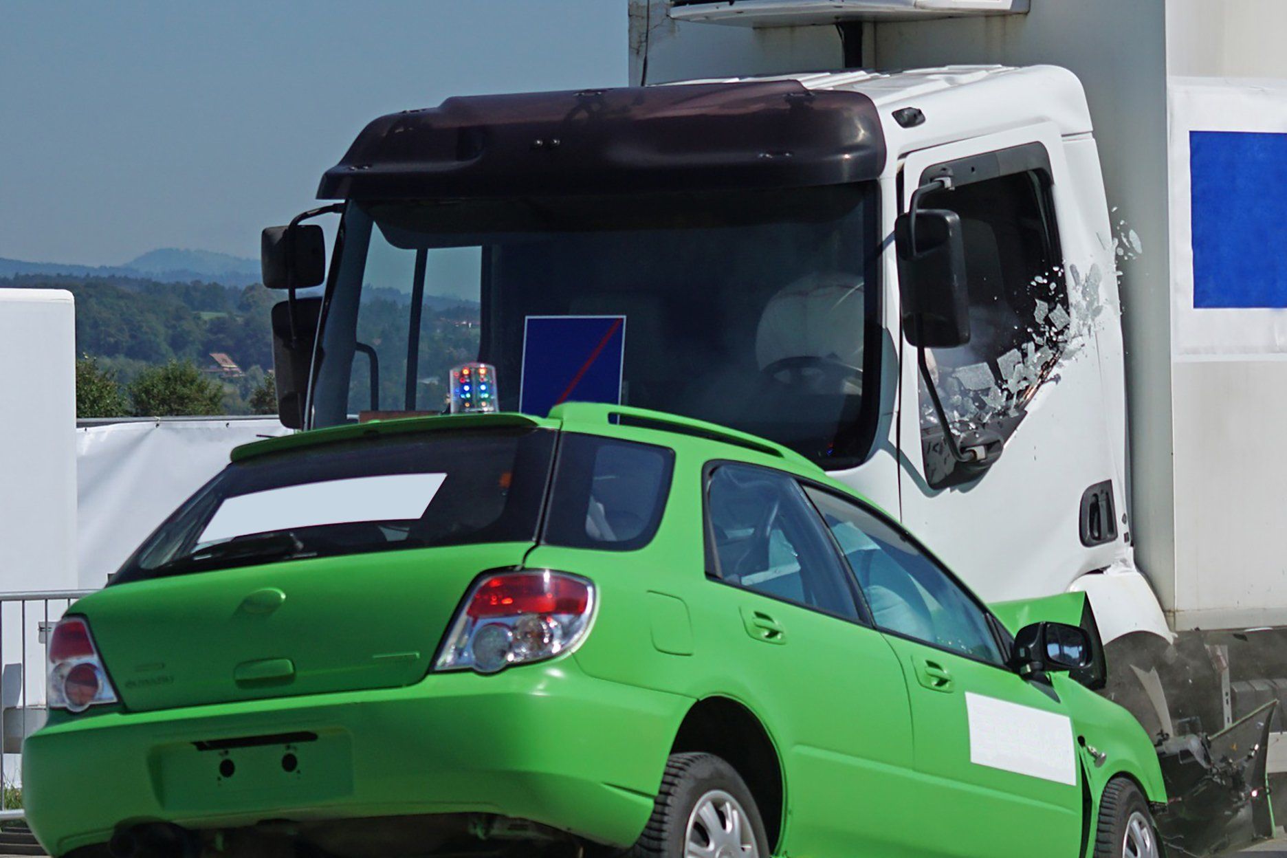 Green car crushed by a large white truck; a crash test demonstration.
