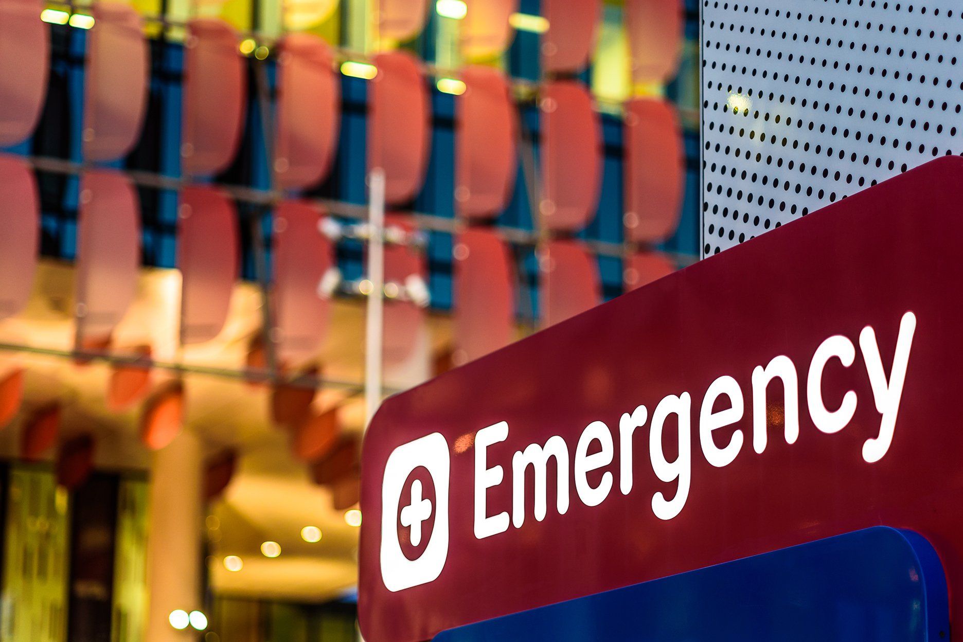 Red emergency sign with white text and a cross symbol in a hospital setting.