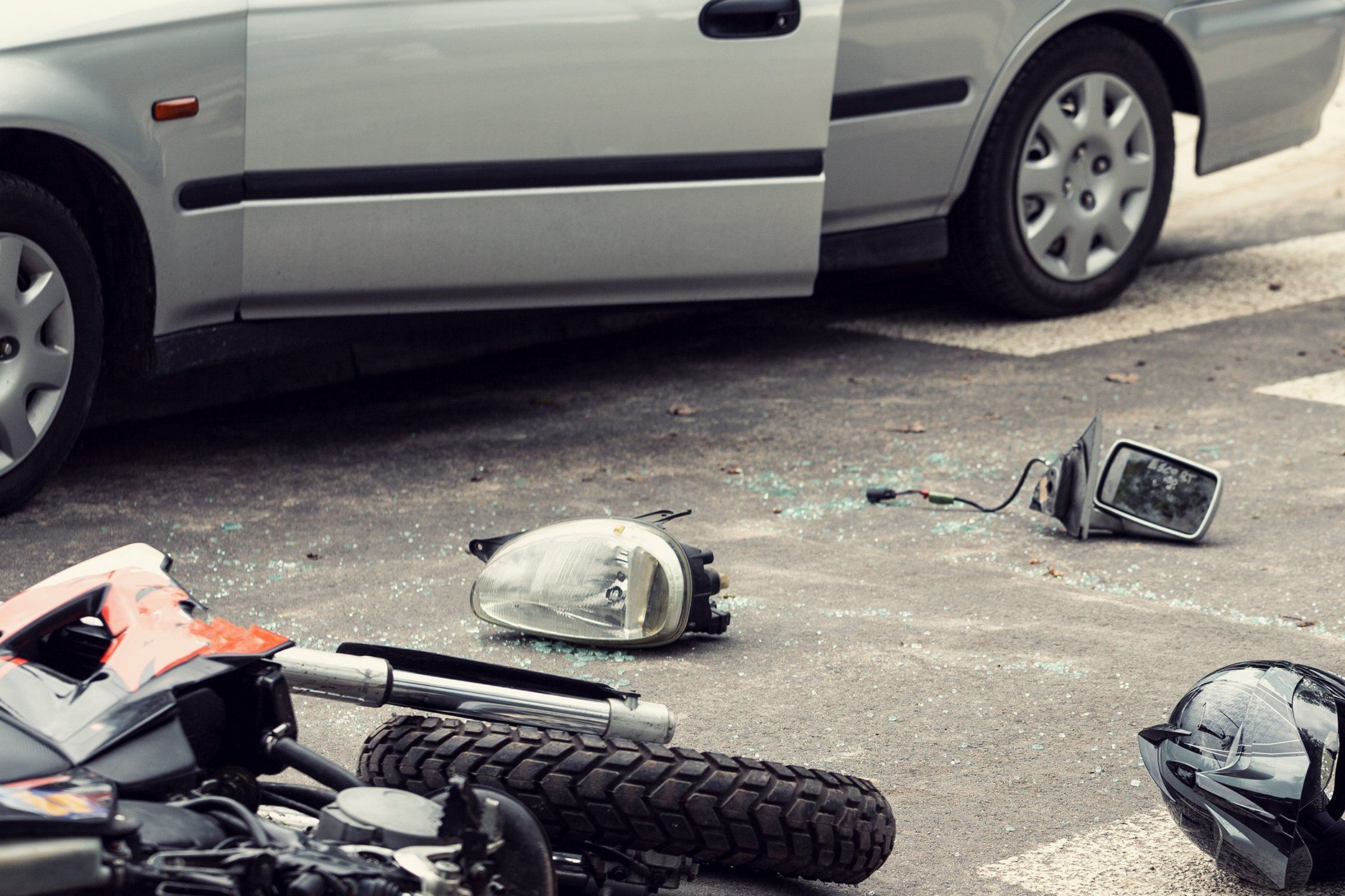 Car and motorcycle crash scene: car door open, motorcycle parts scattered on road.