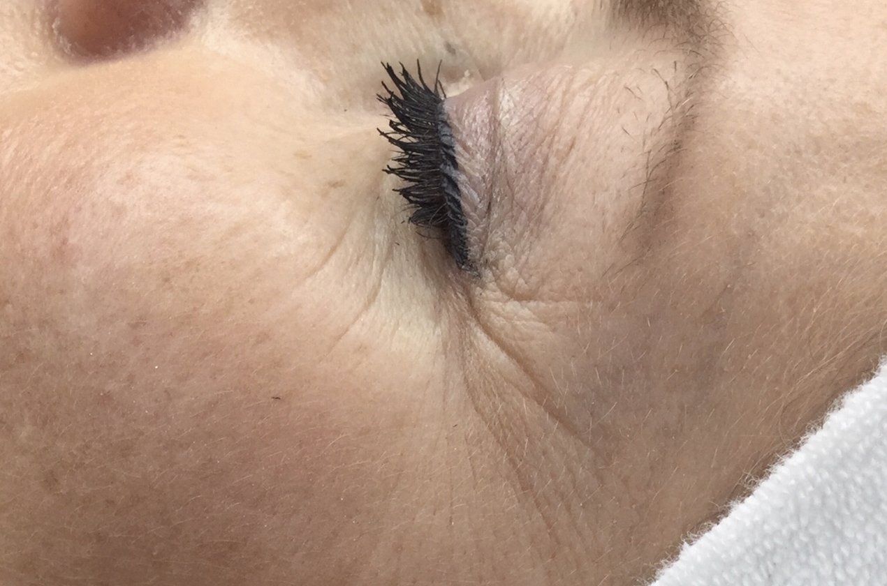 Nahaufnahme eines geschlossenen Auges mit langen Wimpern und einem weißen Handtuch in der Nähe.