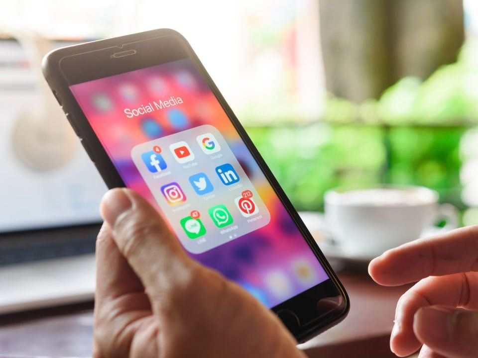 Eine Person hält ein Mobiltelefon mit Social-Media-Symbolen auf dem Bildschirm.