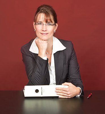 Eine Frau sitzt mit einem Ordner und einem Stift an einem Schreibtisch