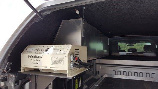 Inside truck bed, a power supply unit is mounted on a shelf. Includes antennas and connections.