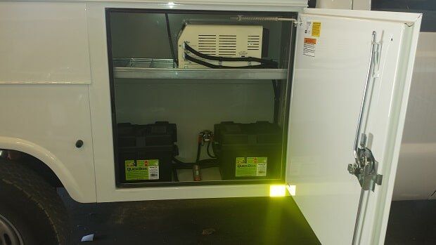 Open white truck compartment reveals batteries and equipment.