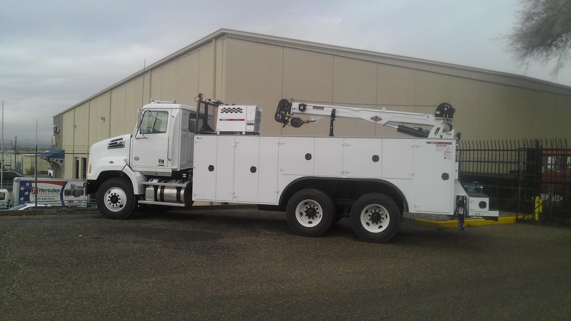 White heavy-duty service truck with crane parked in front of a beige building.