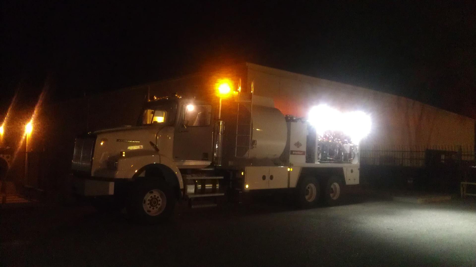 A white service truck with flashing lights at night in front of a large building.