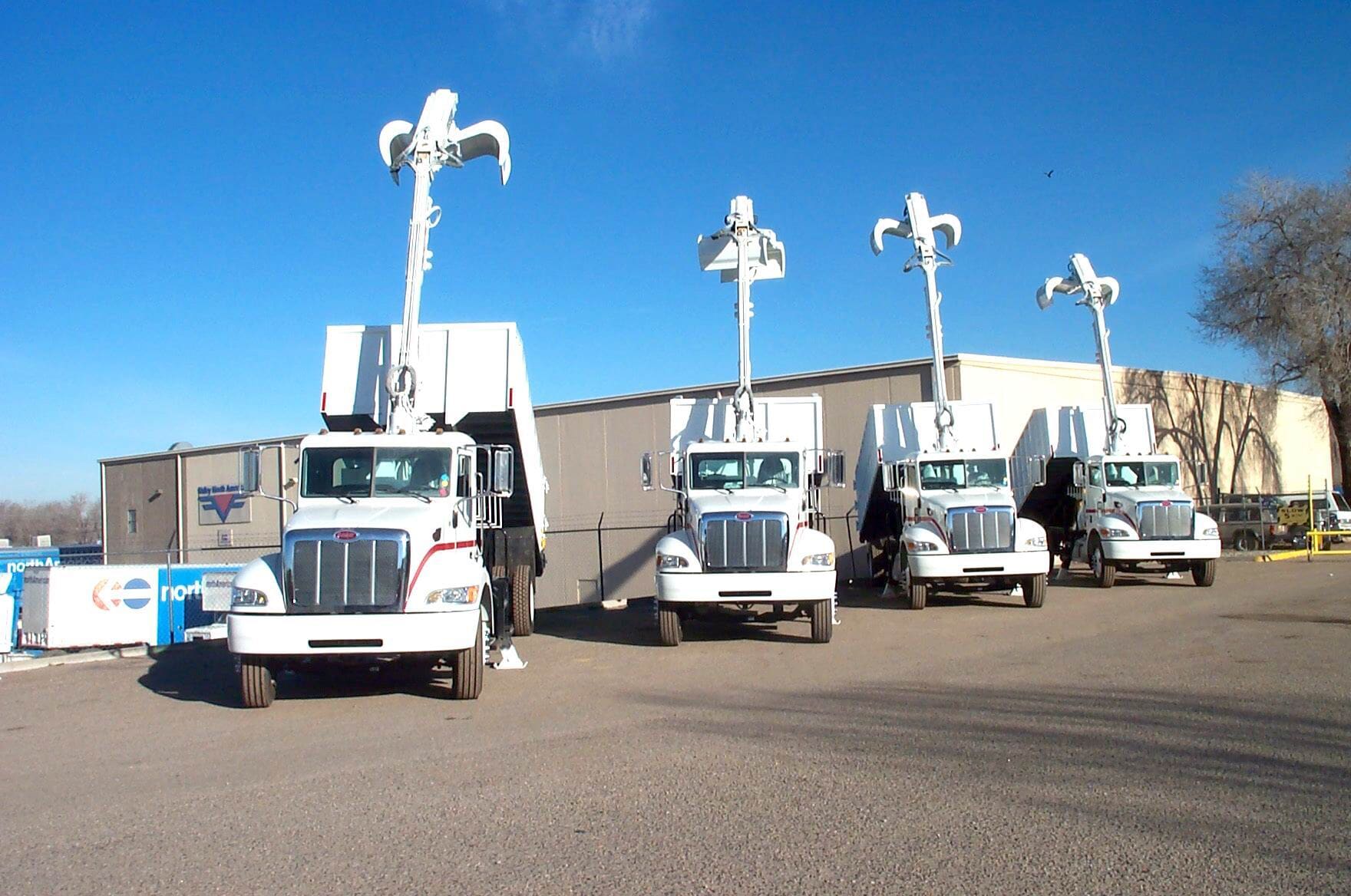 Four white garbage trucks parked in a row, each with a decorative white flourish on top.