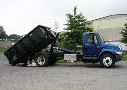 Blue dump truck with raised black dumpster in a paved lot.