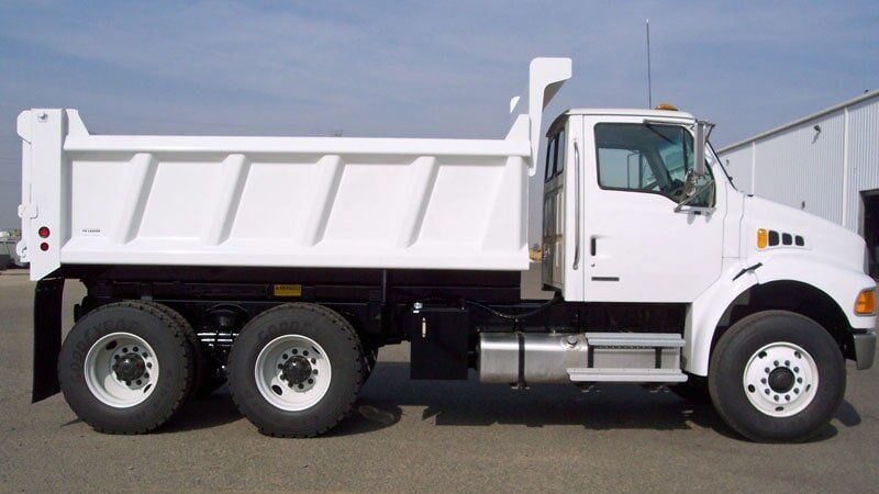 White dump truck on a paved surface, side view, against a building, clear sky.