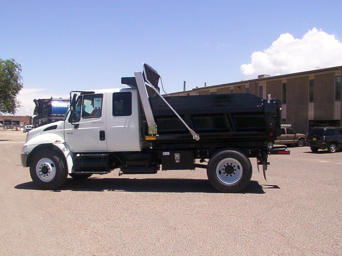 White and black dump truck parked on a paved lot on a sunny day.