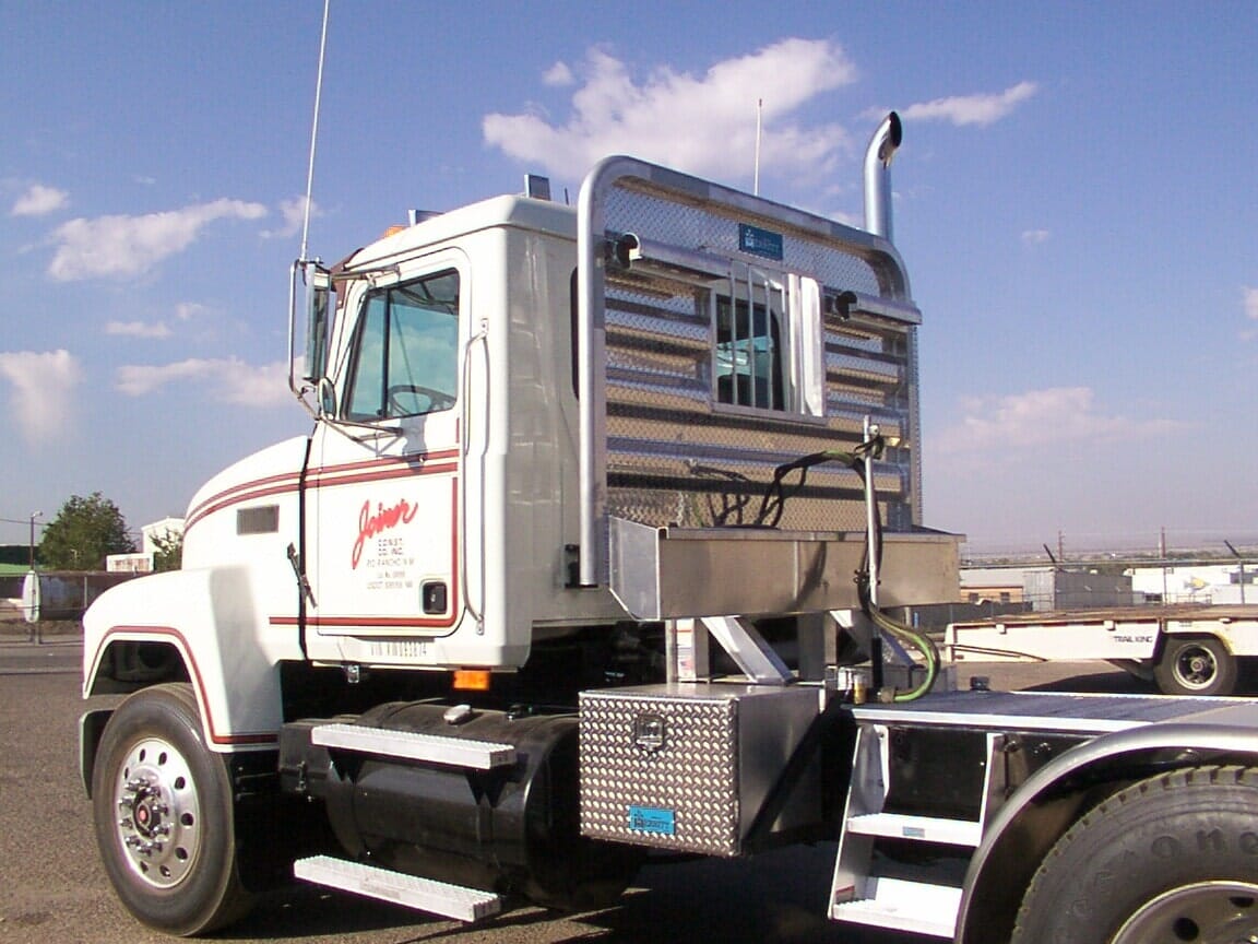 White semi-truck with a custom aluminum headache rack parked on an asphalt lot on a sunny day.