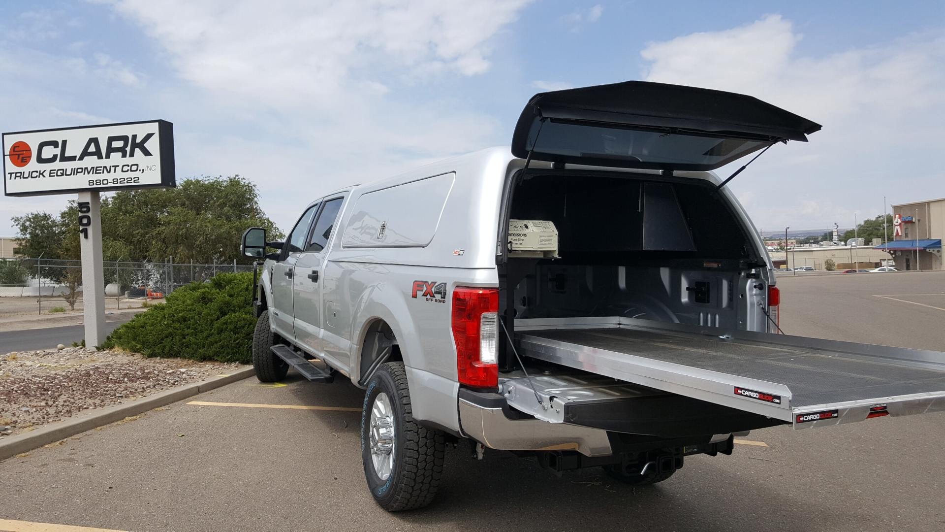 Silver truck with cargo bed extended, parked near a business sign on a sunny day.