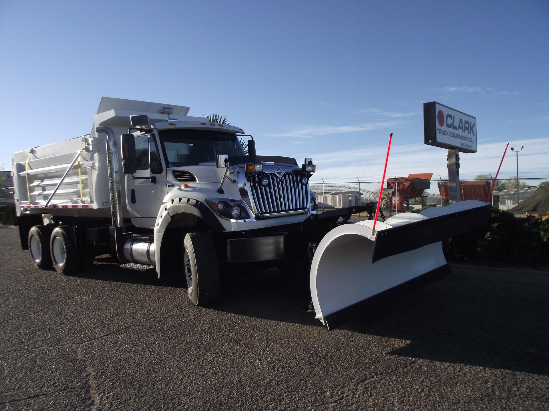 White snowplow truck with the plow lowered, parked in front of a business with a sign.