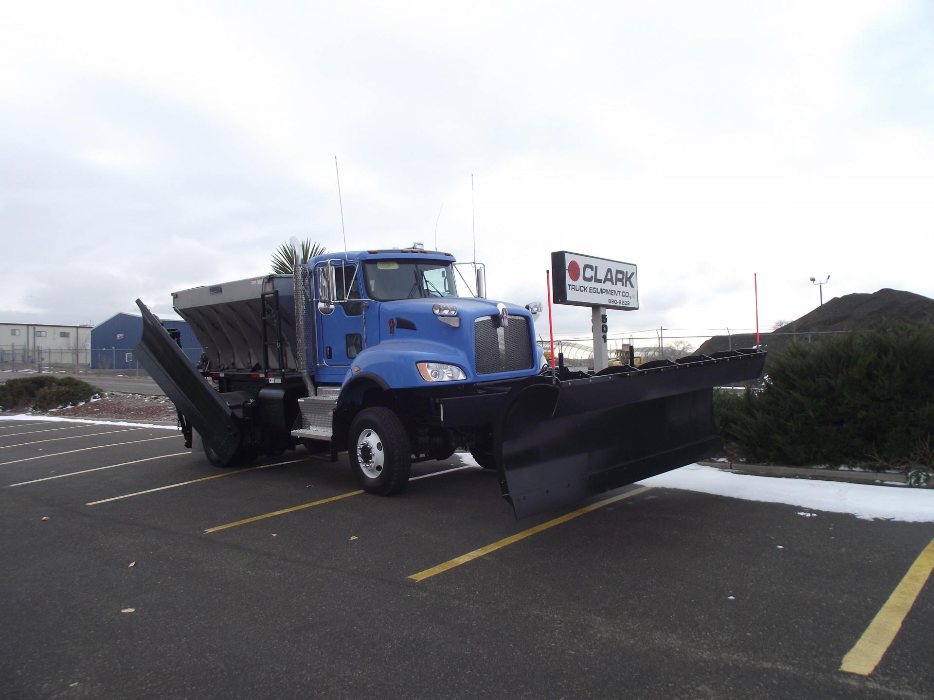 Blue snow plow truck parked in a lot with the plow lowered.