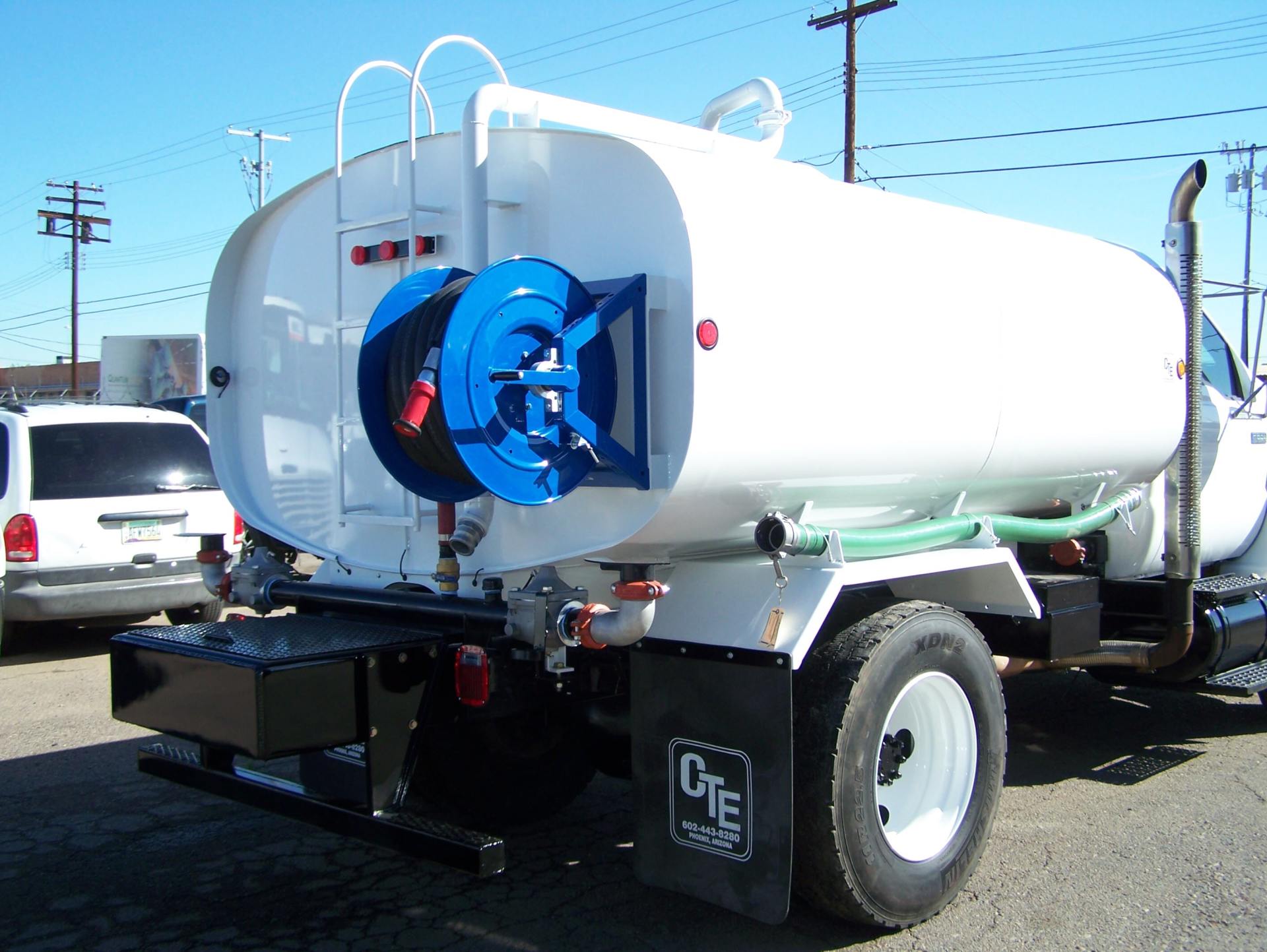 White water tanker truck with blue hose reel, parked outside.