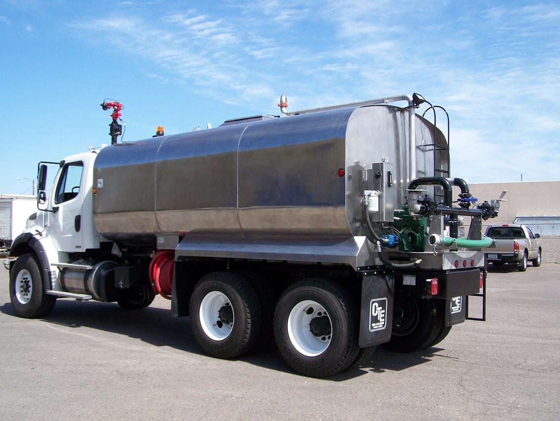 White tanker truck with a stainless steel tank, parked outdoors.