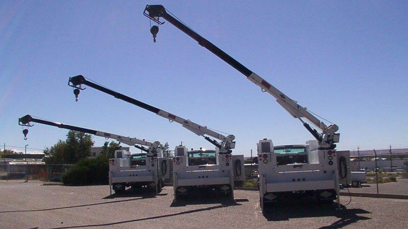 Three utility trucks with extended cranes against a blue sky.