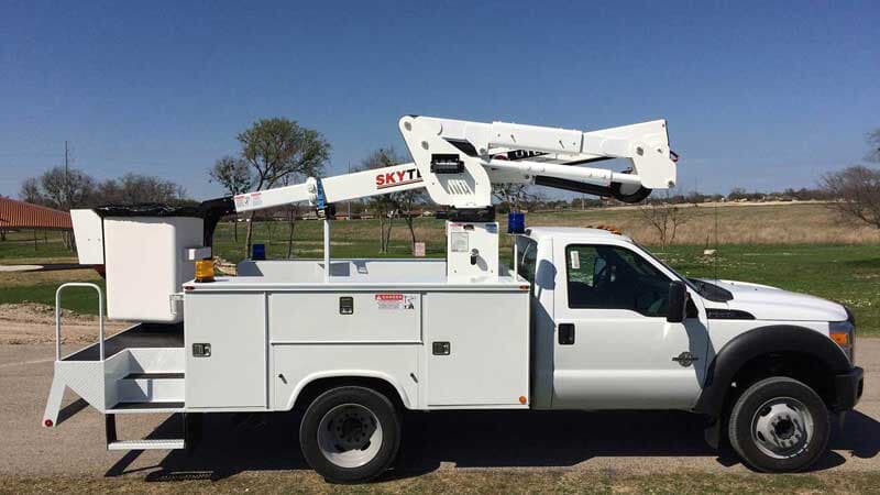 White utility truck with a boom lift on a rural road on a sunny day.