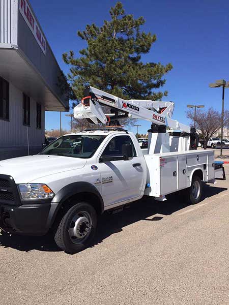 White utility truck with a raised boom, parked outside a building on a sunny day.