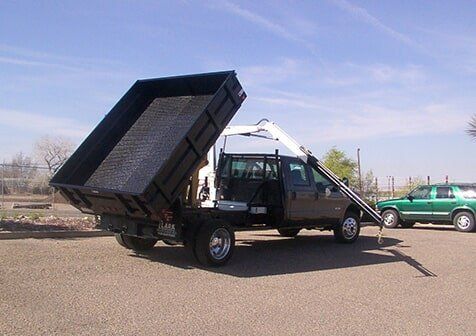 Hoist Truck — Truck Equipment in Albuquerque, NM A dump truck with its bed raised, ready to unload material. The truck is parked on gravel.