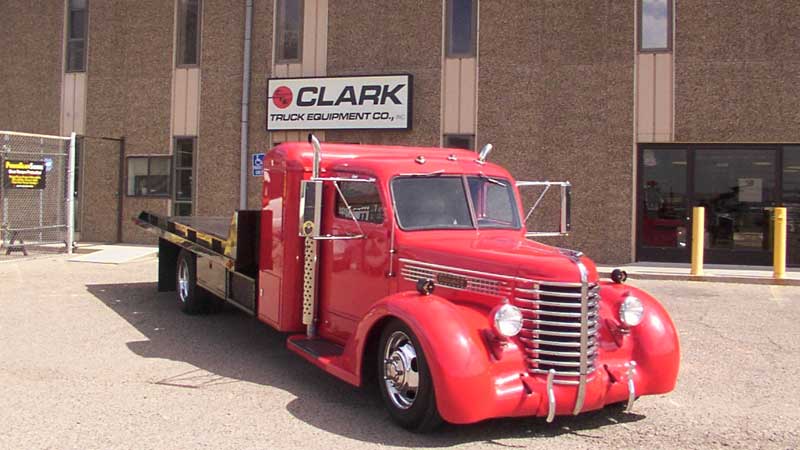 Red vintage tow truck parked in front of the Clark Truck Equipment Co. building.