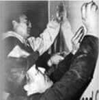 Men in a physical altercation. One holds a glass above another, who is being grabbed. Black and white.
