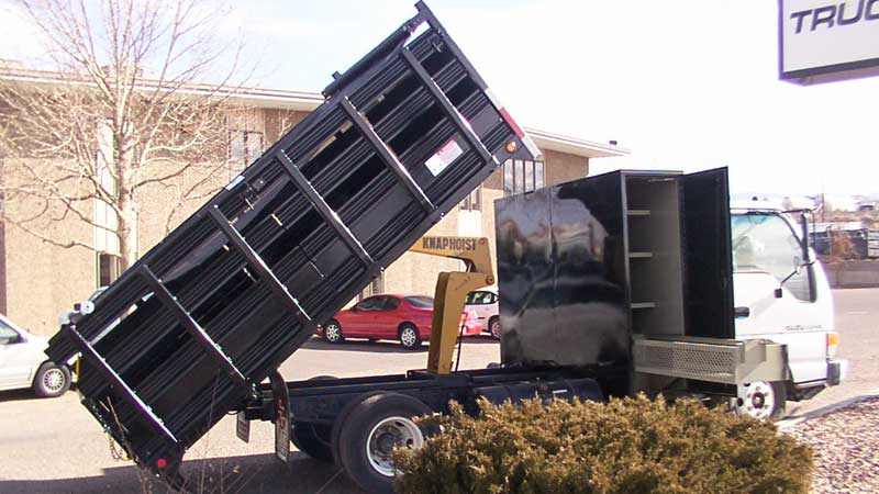 Black dump truck with its bed raised, parked outdoors.