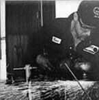 Man in uniform works on something outdoors; black and white photo.