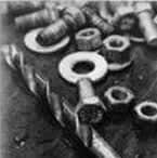 Bolts, nuts, washers, and a drill bit are arranged on a surface in black and white.