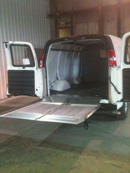 White cargo van with open back doors and ramp, parked inside a building.