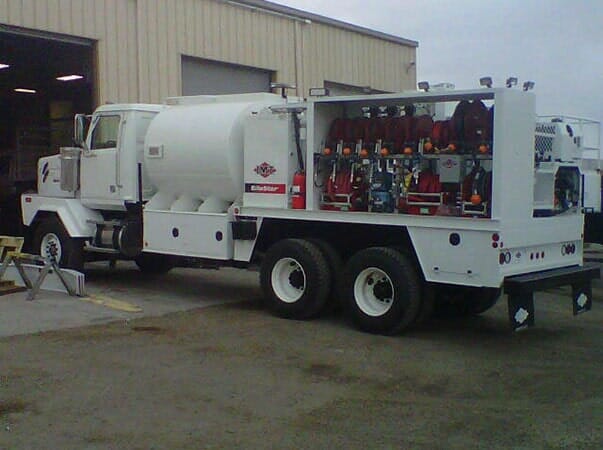 White tanker truck with emergency equipment storage in an industrial setting.