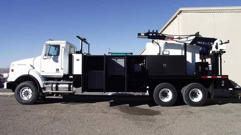 White service truck with black bed, equipment, and tires parked in front of a building on a sunny day.