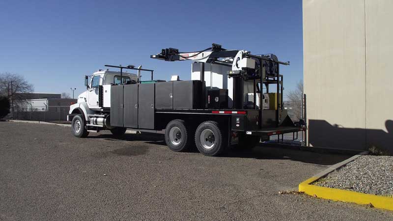 A utility truck with a crane parked next to a building on a sunny day.