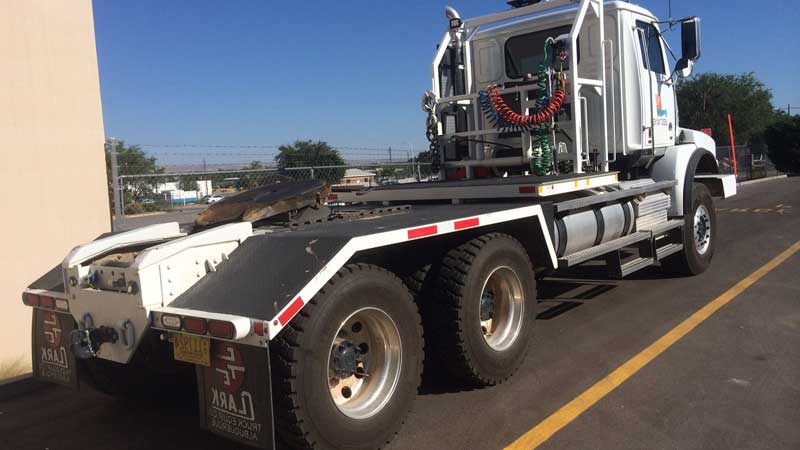 White heavy-duty truck with large tires parked outside on a sunny day.