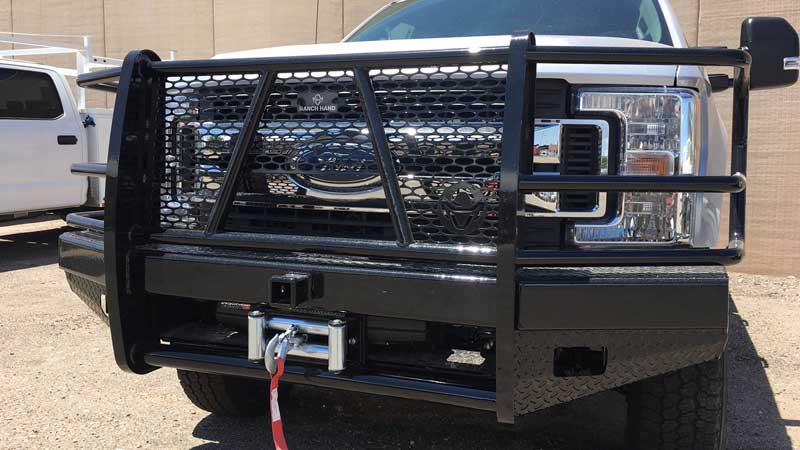 Black Ford pickup truck with a grill guard and winch in a sunny setting.