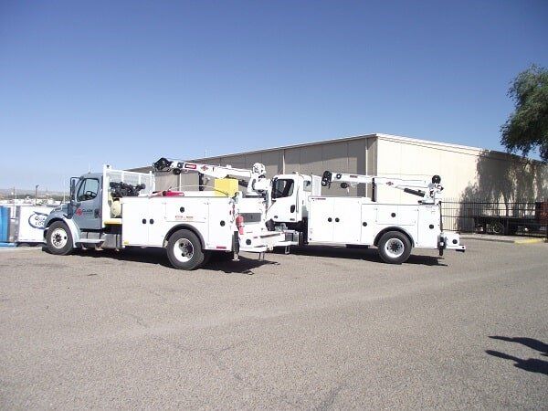 Two white utility trucks parked outside a building on a sunny day.