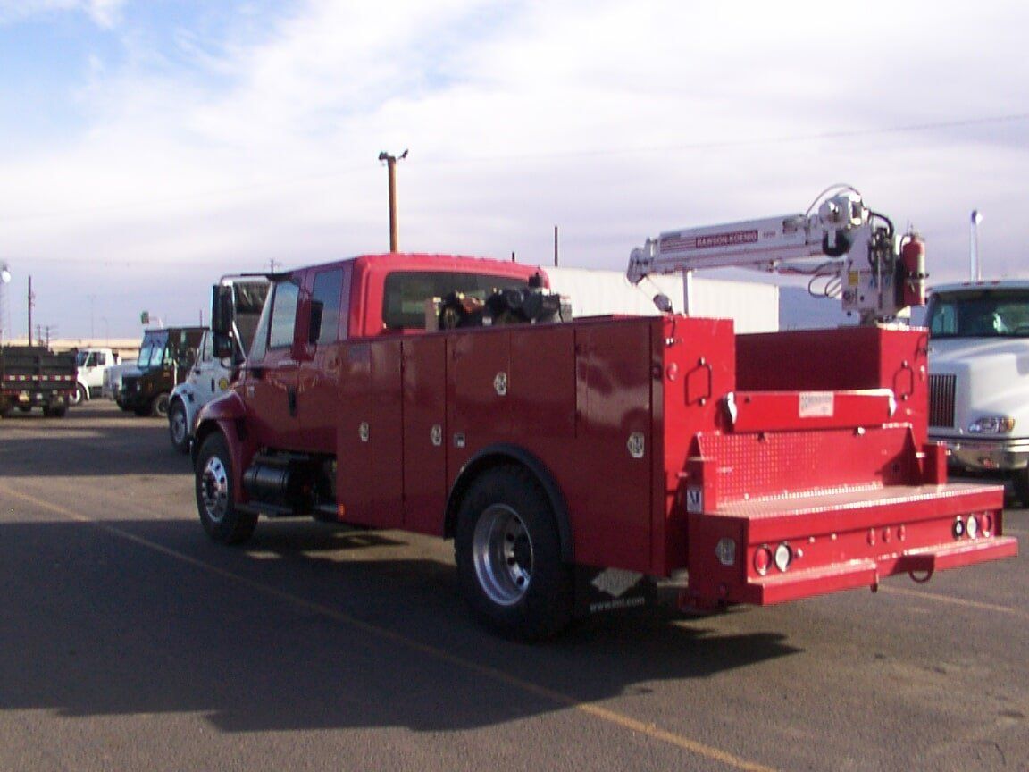 Red work truck with a crane in a parking lot.