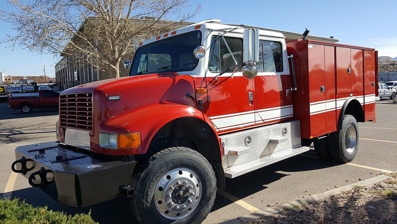 Red and white fire truck with a brush guard parked outdoors.