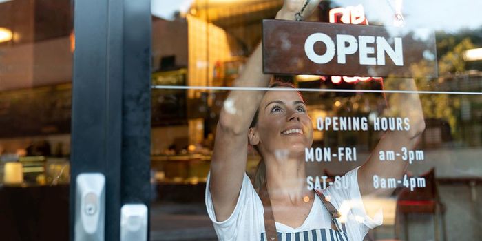 Portrait of a happy business owner hanging an open sign on the door at a cafe and smiling - food and drinks concepts