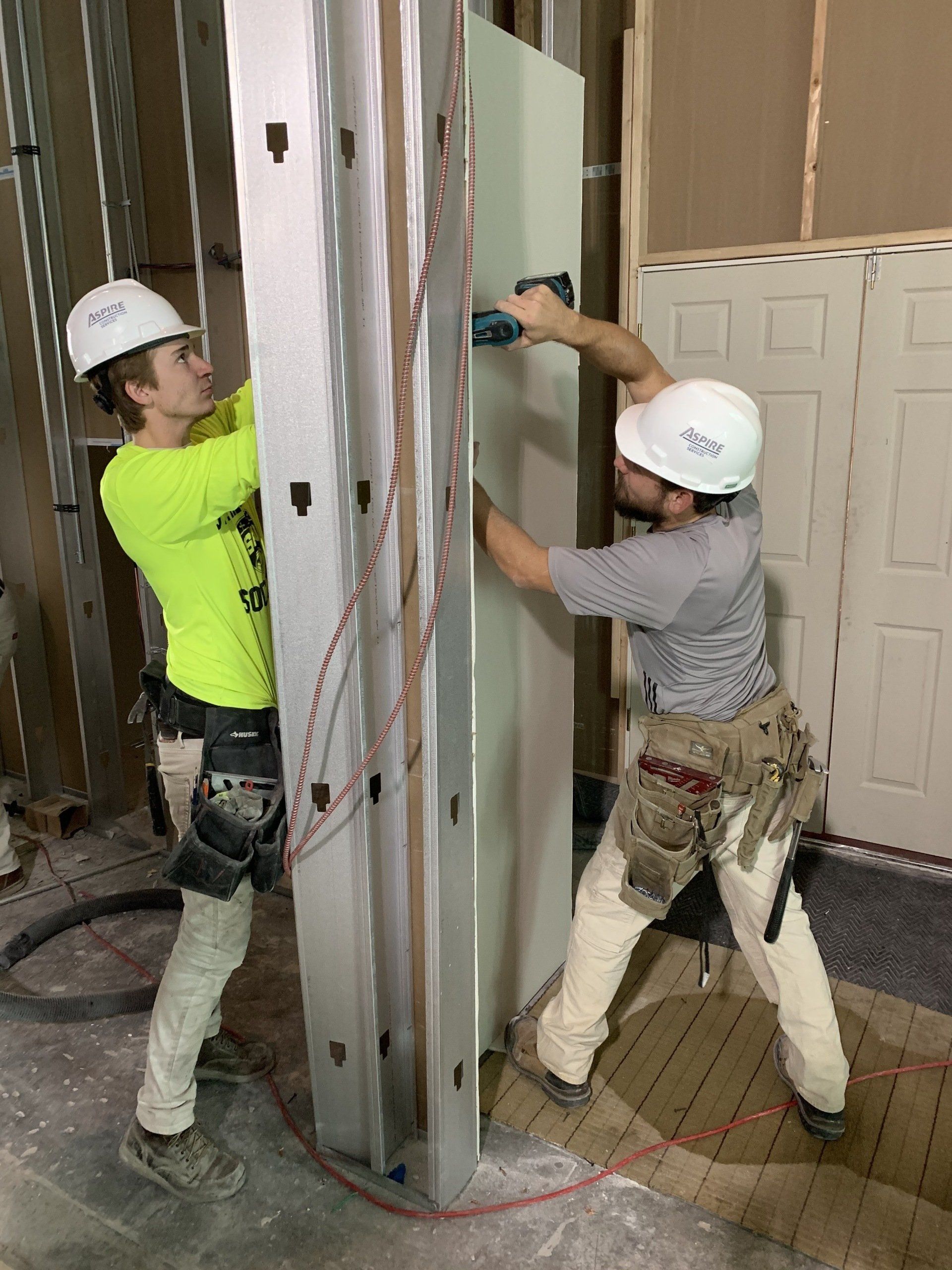 Two workers in hard hats installing a wall panel on a construction site