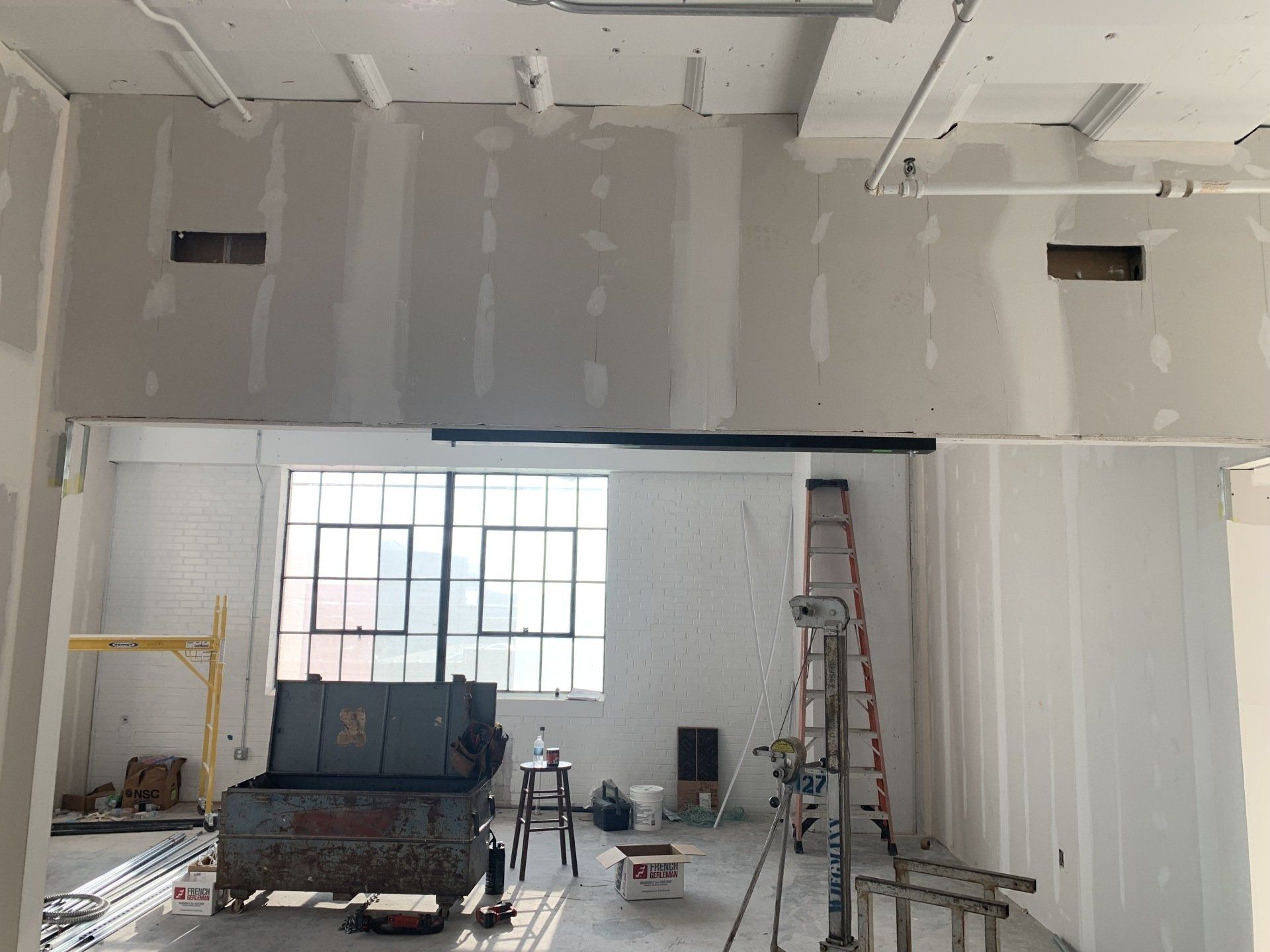 Partially finished interior with drywall, ladders, tools, and a window under construction