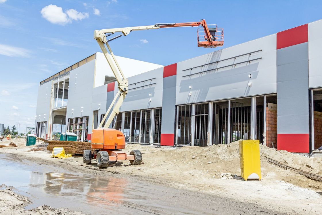 Construction site with white commercial building, orange lift, and workers on a muddy road