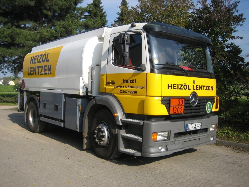 Ein weiß-gelber Heizöl Lentzen Tankwagen parkt im Freien auf einer gepflasterten Fläche.