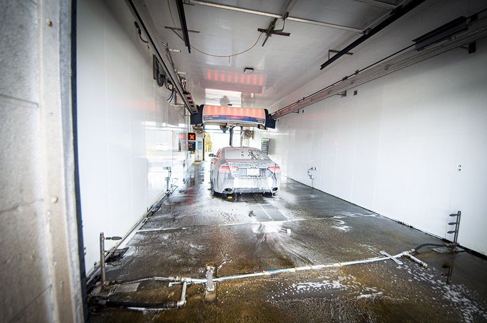 Car being washed in a car wash tunnel with soapy foam.