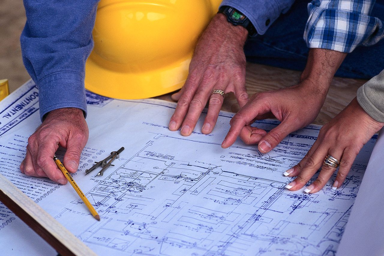 A group of people looking at a blueprint with a yellow hard hat in the background