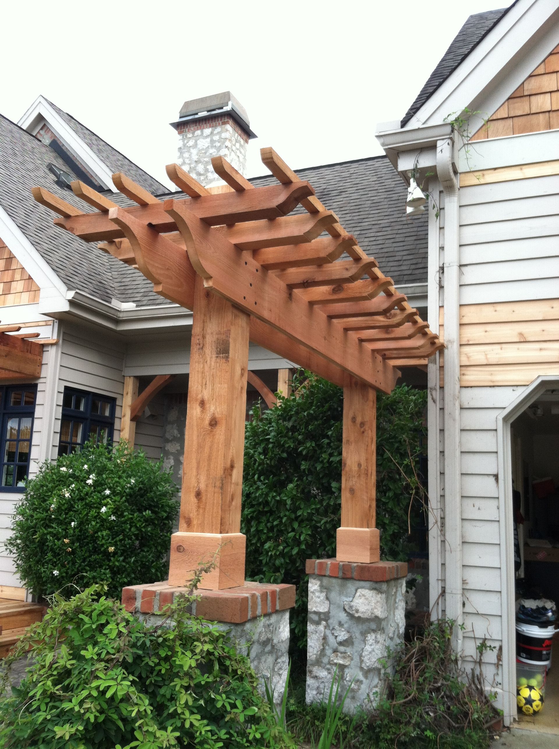 A wooden pergola is attached to the side of a house.