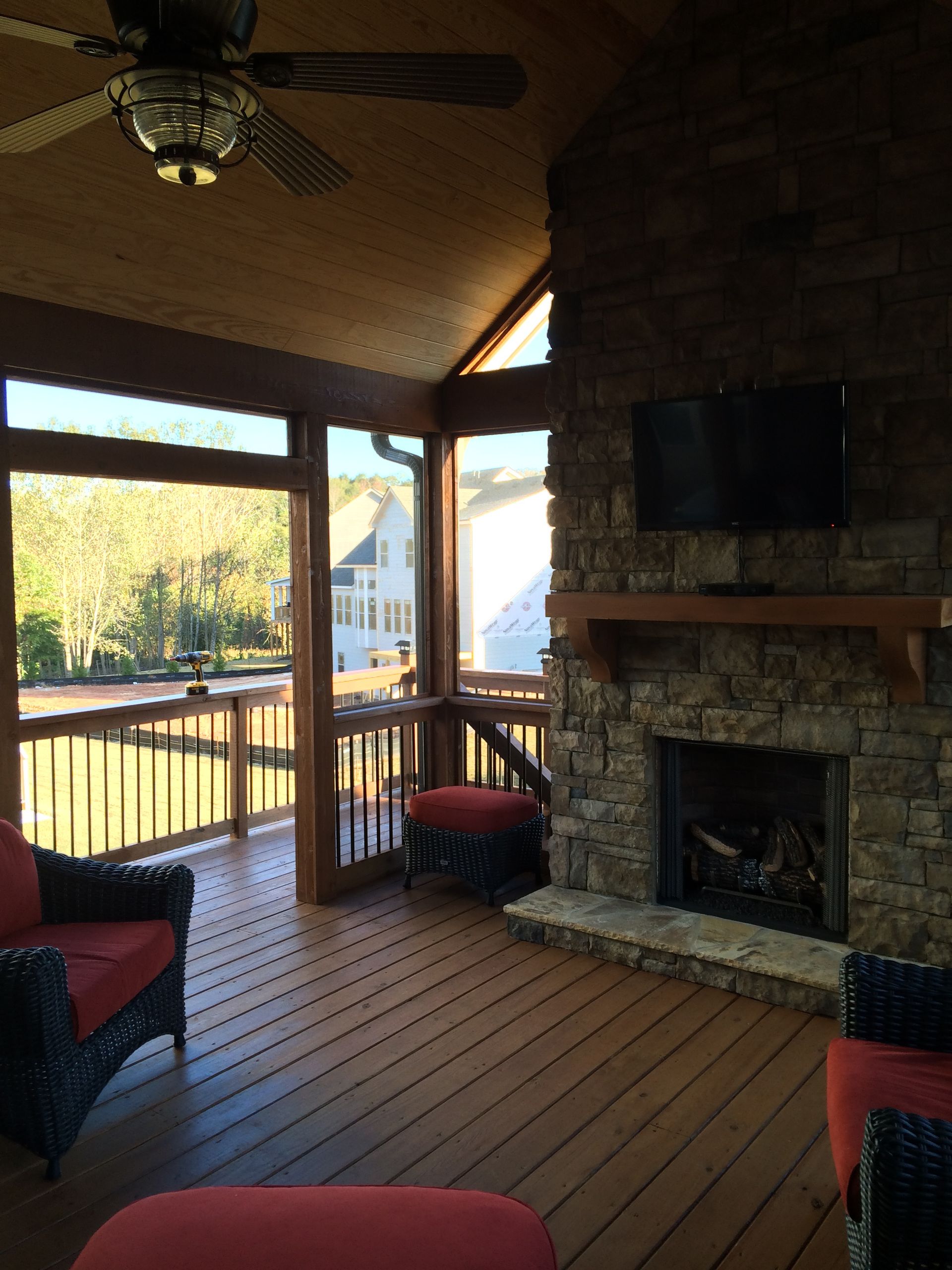 A screened in porch with a fireplace and a ceiling fan